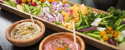 Colorful vegan platter with fresh vegetables including purple cauliflower, golden cherry tomatoes, asparagus, radishes, and broccolini served with hummus and beetroot dip, supporting plant-based nutrition for reproductive health - WeNatal prenatal